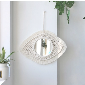 Détail d'un miroir mural macramé en forme d'œil avec franges en coton de couleur ivoire