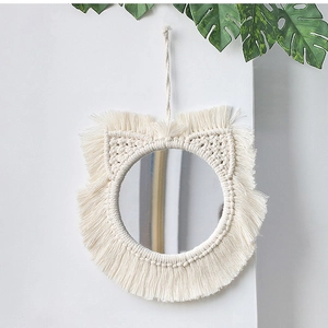 Detail of bohemian woven cotton cat-shaped mirror with fringe tassels on white wall