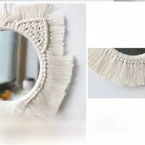 Close-up of handmade macrame mirror with dense bohemian cotton rope tassels on white wall