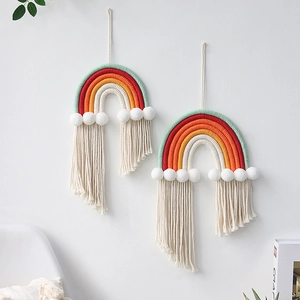 Detail of handmade woven cotton rainbow wall decor with white pom-poms and long tassels