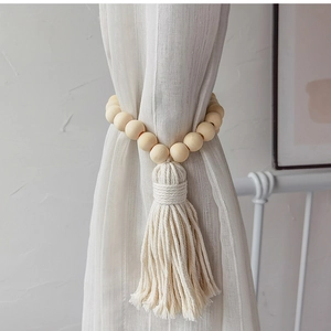 Macro detail of wood bead curtain tieback with cotton tassel on white fabric
