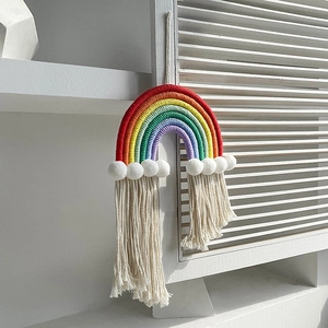 Macro detail of rainbow woven wall hanging with white pom-poms and cream cotton tassels