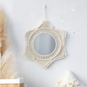 Detalle del espejo redondo de macramé artesanal con flecos bohemios en pared blanca