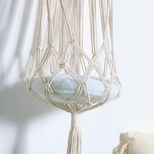 Detail of hand-woven bohemian cat hammock with soft white plush cushion and boho tassels