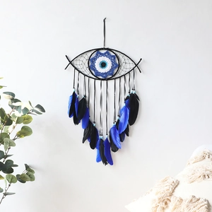 Evil eye wall hanging with blue feathers and beads on a minimalist white wall background