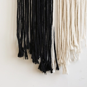 Close-up of black and white hand-woven cotton ropes with tassel detail for wall hanging