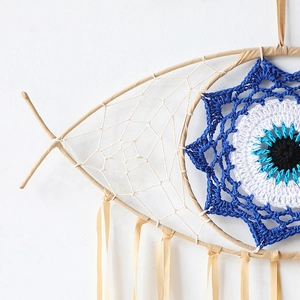 Detailed close-up of fish-shaped dream catcher with woven evil eye and satin ribbons