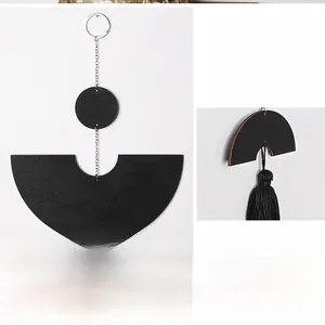 Detail of black geometric wood wall hanging with metallic chains and textile tassels