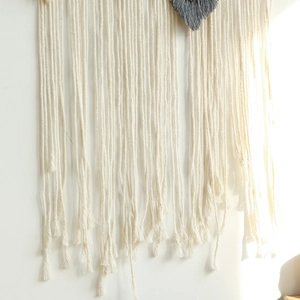 Detail of bohemian hand-woven wall hanging with white cotton tassels and grey heart knot