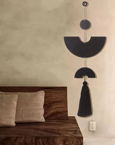 Detail of minimalist black circular wood wall decor with metallic chains and silk tassels