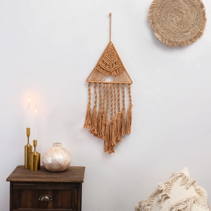 Dettaglio di un arazzo macramè boho triangolare con frange su una parete bianca