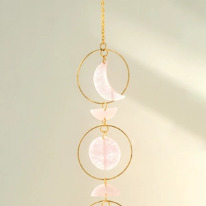 Detail of pink moon phase wall hanging with golden metal chain and acrylic elements