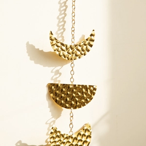 Close-up of hammered gold metal moon phase wall hanging with delicate link chains