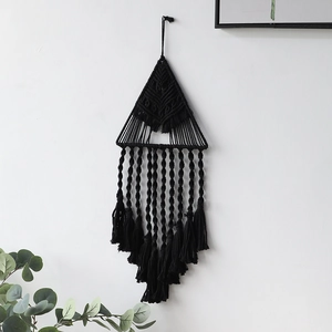 Dettaglio della decorazione murale in macramè nero con trama a triangolo e lunghe nappe