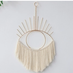Detail of bohemian gold metal eye wall hanging with white cotton rope tassels