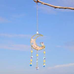 Detail of moon crystal suncatcher with pink natural stone chips hanging against blue sky