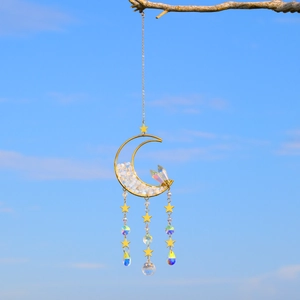 Detail of moon suncatcher with golden metal frame and crystals against a blue sky