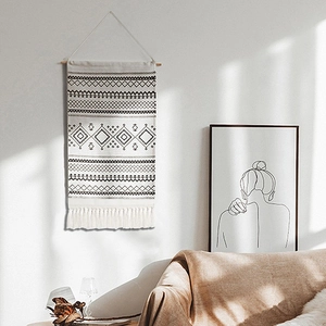 Bohemian handwoven tapestry with black geometric patterns and white tassels on wall