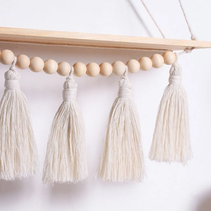 Detail of bohemian wooden bead garland with cotton tassels hanging from a wood shelf