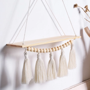 Detail of bohemian wooden wall shelf with white cotton tassels and beads decoration