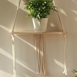 Detail of Bohemian hand-woven macrame wall shelf with natural wood board and soft cotton tassels