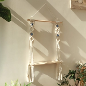Detail of handmade boho macrame wall shelf featuring cotton rope and blue evil eye beads