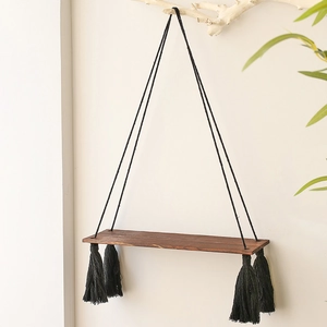 Detail showing the dark brown wood grain surface and black tassel fringe of the boho shelf