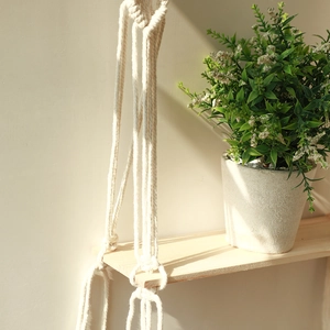 Detailed close-up of handmade macrame cotton rope wall shelf with natural wood board