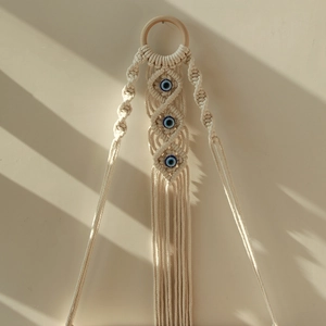 Bohemian handmade macrame wall hanging with evil eye beads and tassels on a neutral wall