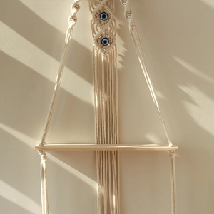 Close-up of handmade macrame wall shelf with wood board and blue evil eye beads