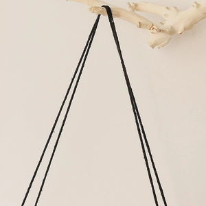 Detailed macro of handwoven black macrame cords on a natural raw wood branch support