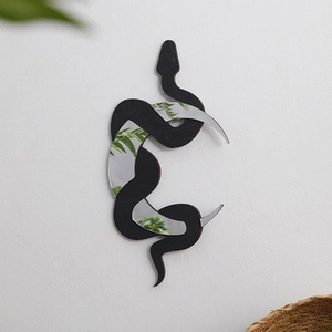 Detail of snake shaped wall mirror with black wood base reflecting green plants