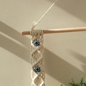 Close-up of bohemian macramé wall hanging with blue evil eye beads on wood pole