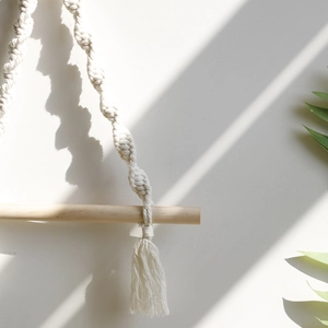 Bohemian handmade cotton wall hanging with woven tassels on a natural wooden stick