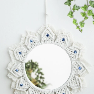 Detail of handmade boho evil eye macrame wall mirror hanging on a white wall