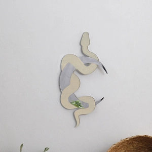 Detail of snake-shaped wall mirror with gold and silver acrylic surface on white wall