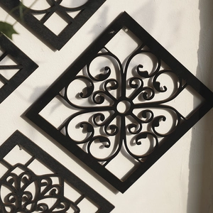 Close-up of black square carved wood wall plaque with intricate floral scroll pattern