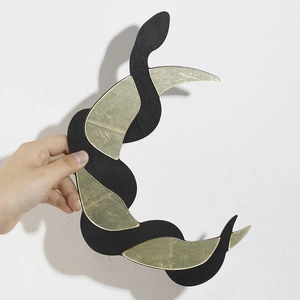 Detail of bohemian wooden snake wall decor with golden crescent mirror accents held by hand