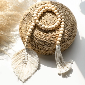 Detail of bohemian wooden bead curtain tieback with white cotton tassel and leaf charm
