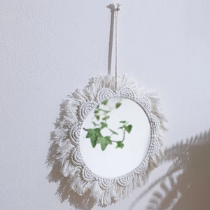 Detail of bohemian woven macrame mirror with fringe on a minimalist textured wall