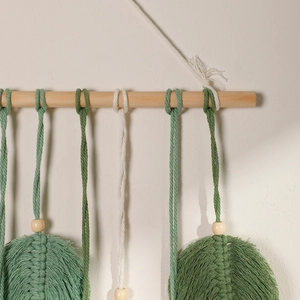 Detail of bohemian macramé wall hanging with green cotton feathers and wood beads