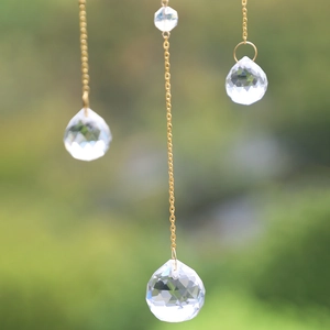 Detailed view of multifaceted crystal suncatcher pendant with gold chain hanging outdoors