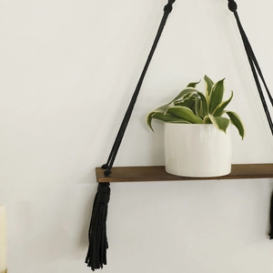 Bohemian black macrame wall hanging shelf with dark wood board and tassel detail