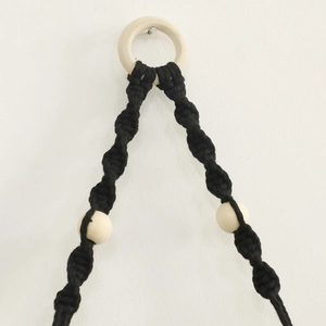 Detail of bohemian black hand-woven macrame plant hanger with wooden ring and beads
