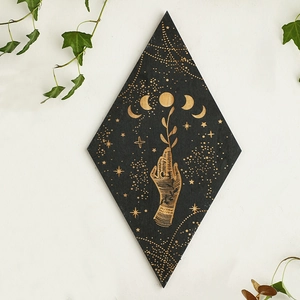 Detail of black diamond-shaped wall decor with golden moon phases and botanical hand carving