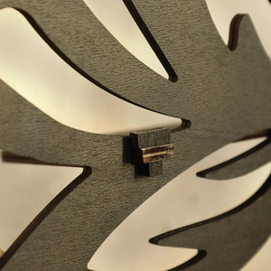Close-up of laser-cut monstera leaf pattern on dark grey wooden crystal display shelf