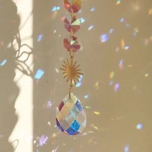 Detail of crystal suncatcher with golden sun motif casting rainbow light on white wall