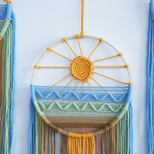 Handmade macrame wall hanging with woven sunrise landscape in a round wooden frame