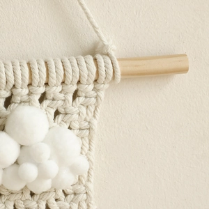 Détail de la texture du tissage en coton et des pompons sur le support en bois mural