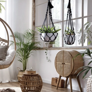 Detail of two black bohemian hand-woven macrame plant hangers hanging by a window